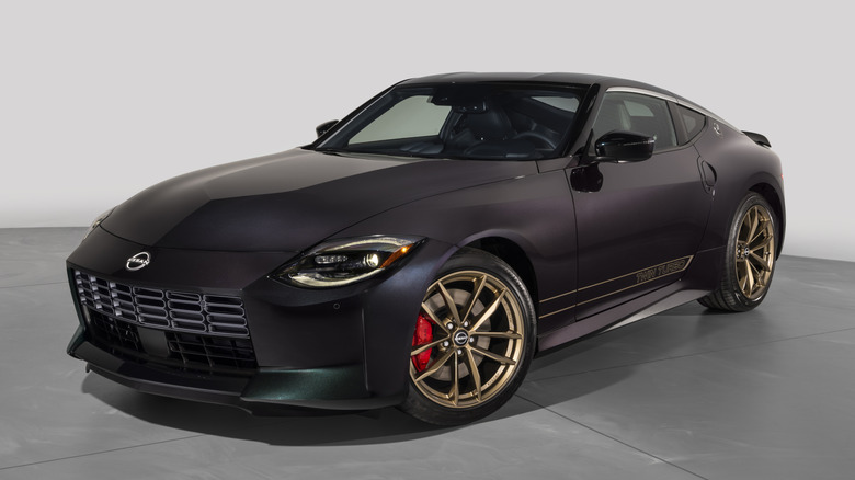 Front three quarters shot of a dark Nissan Z with gold wheels parked on a concrete floor in front of a blank gray background