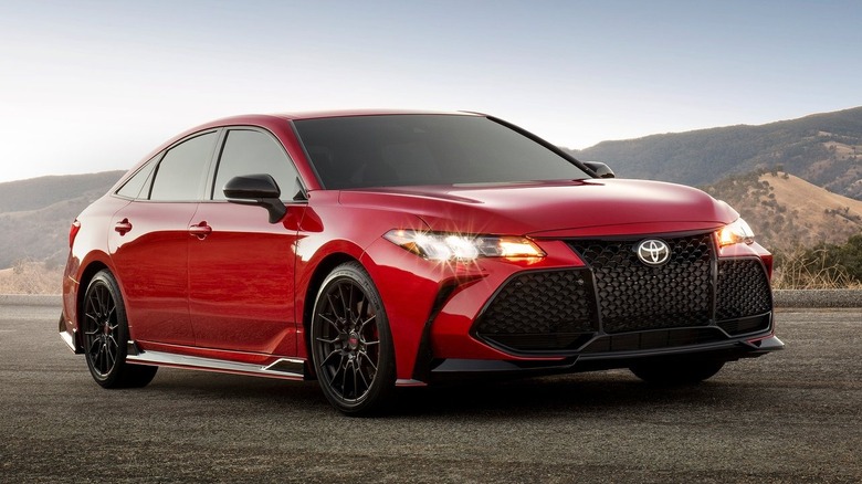 Front three quarters shot of a red Avalon TRD parked ion asphalt in front of mountains