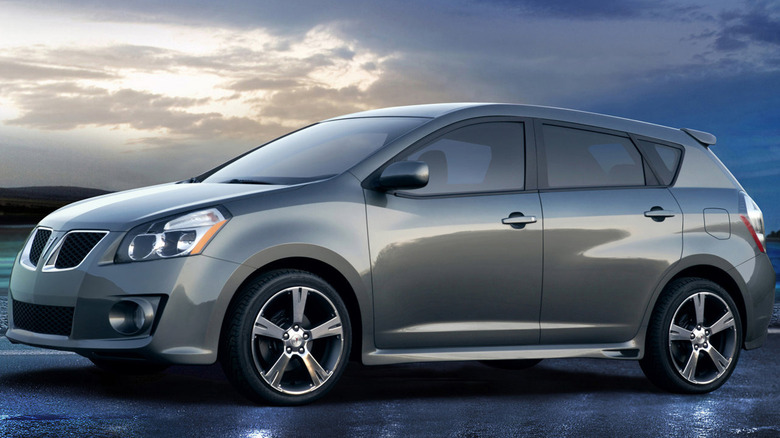 Side view of a gray second-generation Pontiac Vibe parked on wet asphalt in front of a moody cloudy sky