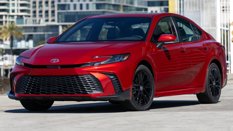 Supersonic Red 2026 Toyota Camry parked on a paved surface with a city skyline in the background