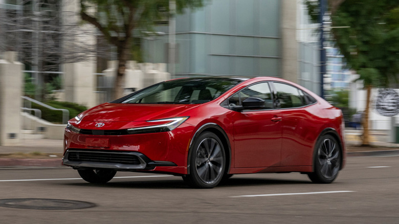 Supersonic Red 2026 Toyota Prius XLE driving down city street next to a building