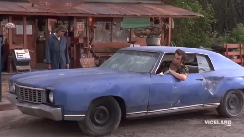 Ace Ventura stopped in front of a gas station while driving his blue 1972 Chevrolet Monte Carlo