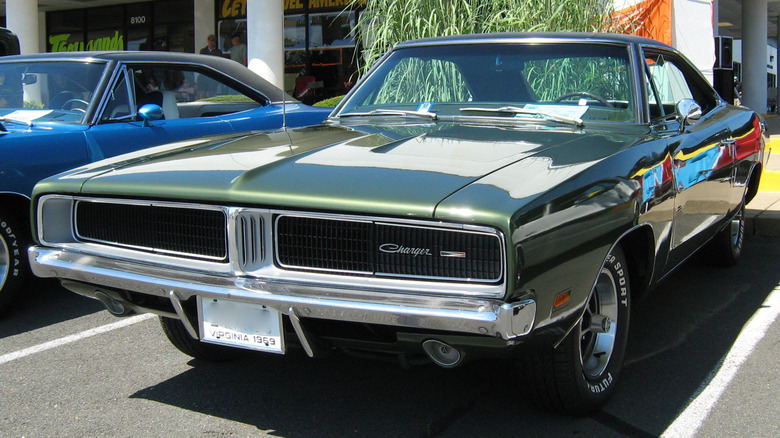 Green 1969 Dodge Charger coupe seen from front left parked outdoors beside another vintage Dodge