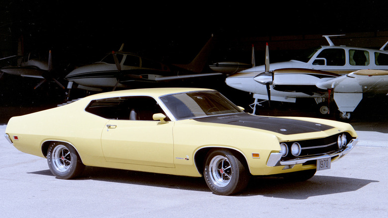 Yellow 1970 Ford Torino Cobra seen from left front parked in front of airplanes
