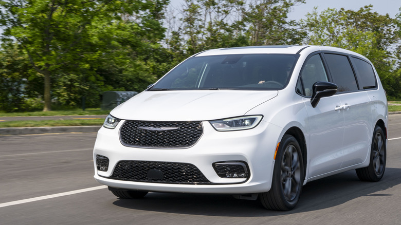 front three quarters shot of a white Chrysler Pacifica driving past grass and trees