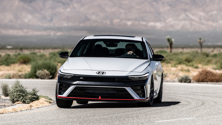 front three quarters shot of a white Elantra N driving around a corner in the desert in front of mountains and Joshua Trees
