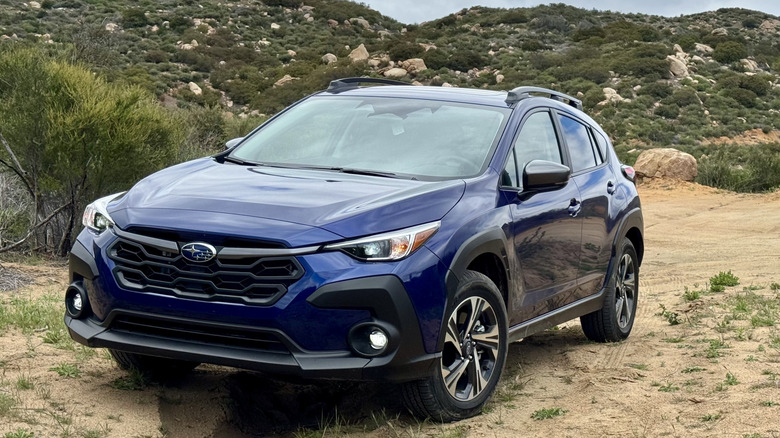 front three quarters shot of a dark blue Subaru Crosstrek parked on dirt in front of green rocky mountains