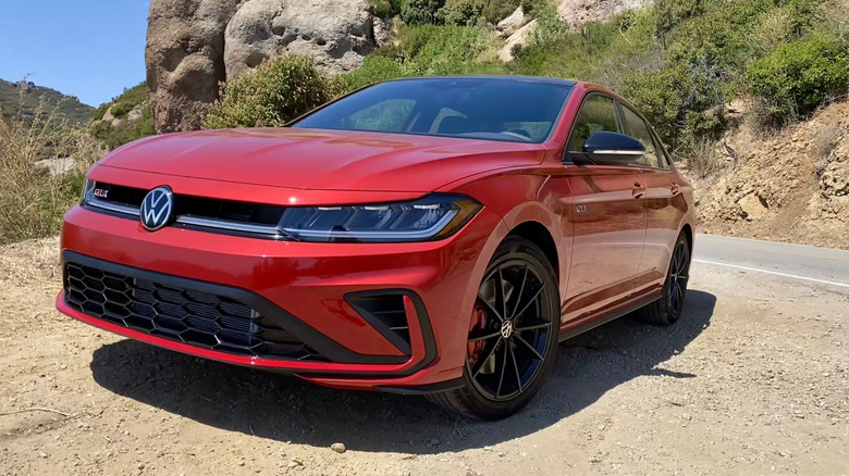 front three quarters shot of a red Volkswagen Jetta GLI parked on dirt in front of a shrub covered rock mountain face