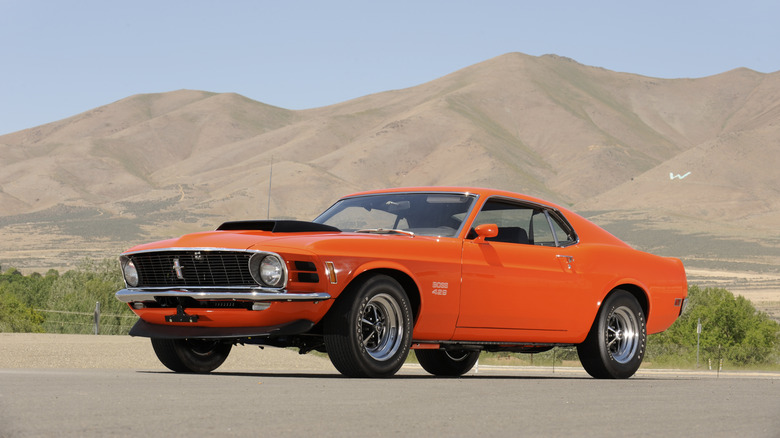 An orange Ford Mustang Boss 429 sitting on pavement with mountains in the background.