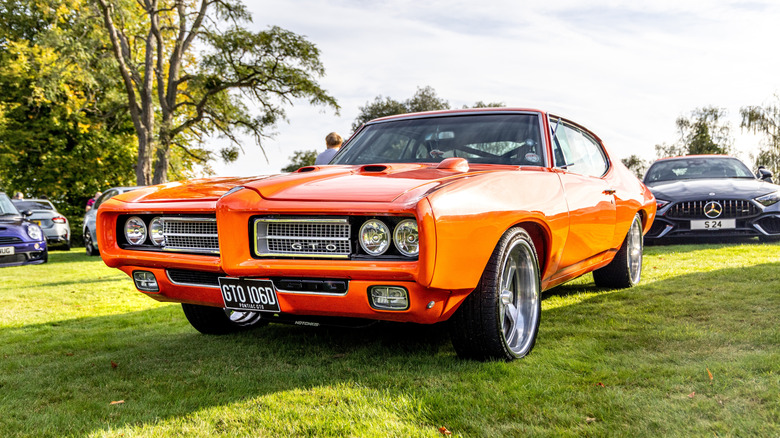 An orange Pontiac GTO Judge parked on grass with other cars in the background.