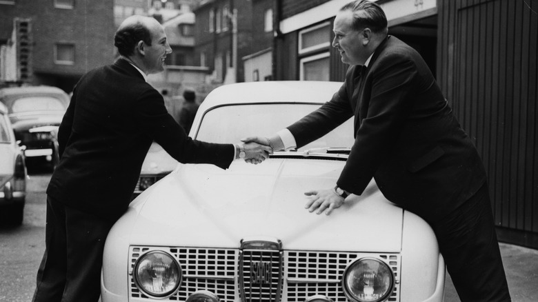 British racing driver Stirling Moss (left) shaking hands with his brother-in-law Erik Carlsson over the bonnet of a SAAB car, as the pair prepare to take part in the East Africa Safari Rally, Piccadilly, London, February 25th 1965. (Photo by Kent Gavin/Keystone/Getty Images)