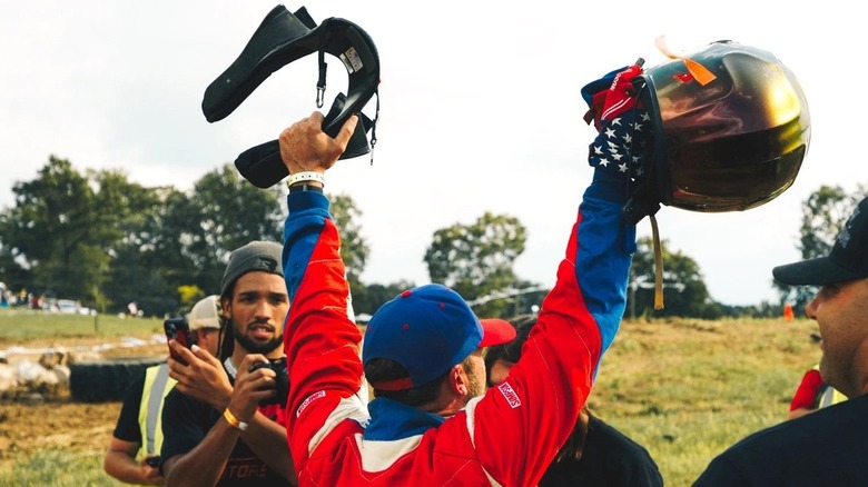 A racer shows off his helmet and HANS device post-race celebration.