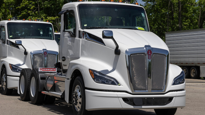 A pair of white Kenworth T680 semi-trucks on a parking lot