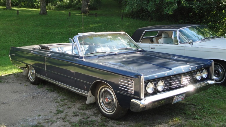 Front 3/4 view of a blue1965 Mercury Park Lane Convertible parked on grass with another car in the background