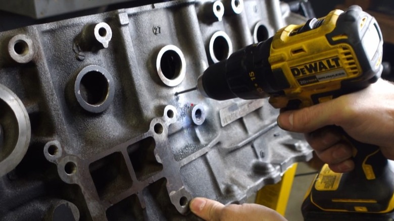 A person's hand holding a drill as it drills into an engine block