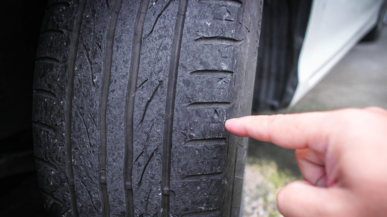 A person pointing toward a worn-out tire mounted on a white passenger vehicle.