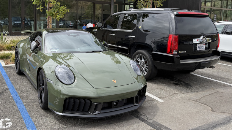 A green Porsche 911 Carrera GTS next to a black Cadillac Escalade hybrid