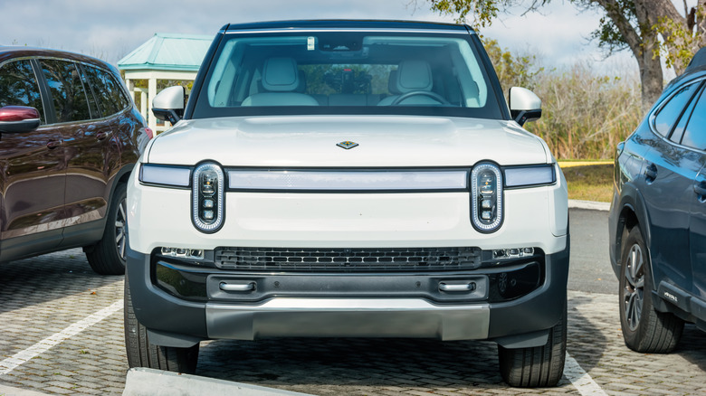 A front-end view of a parked white Rivian R1S without front license plates.