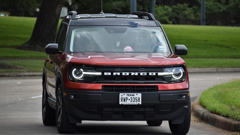 A red Ford Bronco Sport with a Texas license plate driving down a suburban street.