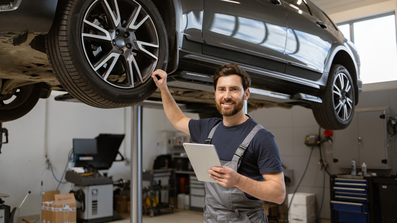 Mechanics working on car maintenance in modern auto repair shop, using laptop and tools. Auto repair, service check, and team collaboration displayed.