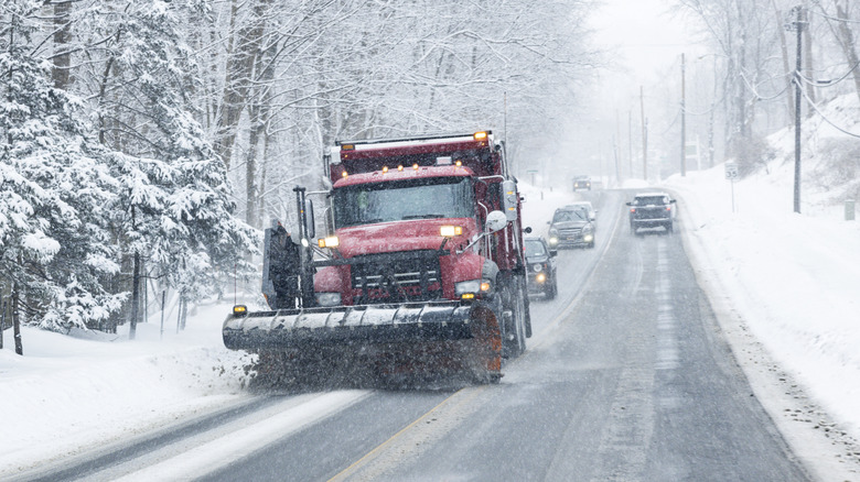 A red snow plow clears the road ahead of some cars.