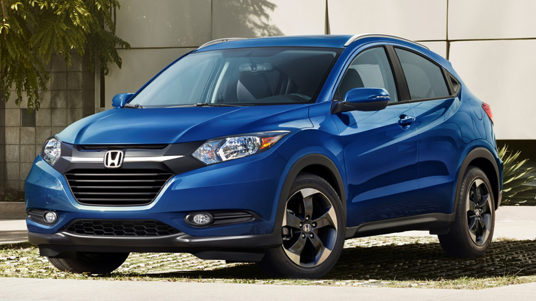 A blue 2018 Honda HR-V sits near a building in the sun.