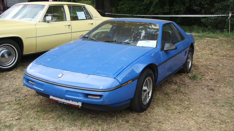 A blue Pontiac Fiero in a grass lot at a car meet