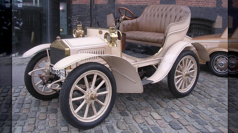Tan 1905 Rolls_royce 10 H.P. seen in left front three-quarter view parked in a cobbled courtyard