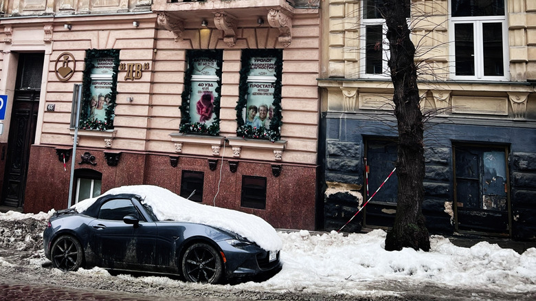 Lviv, Ukraine - February 07, 2026: Historic architecture on a snowy city street with a parked Mazda MX-5 car and leafless tree.