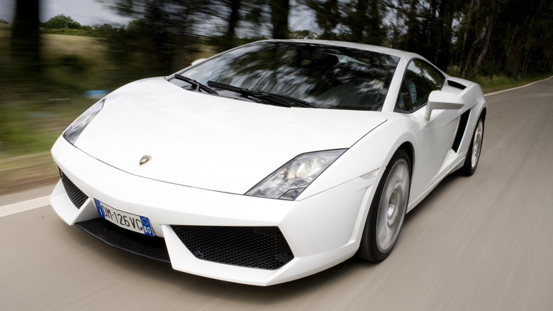A white Lamborghini Gallardo LP 560-4 Coupé driving on a road lined with trees