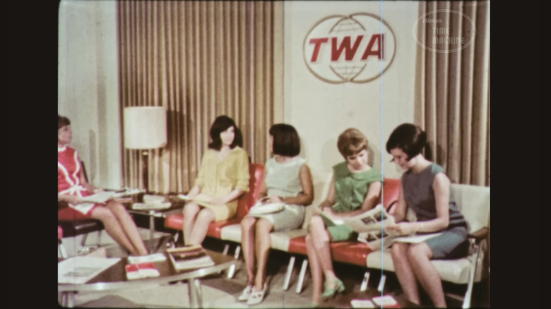 A group of women dressed in late 1960's attire, wait in the white and gold TWA waiting area for their interview in a screenshot of the 1967 TWA recruitment film.