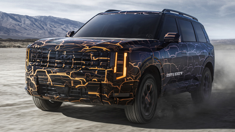 Front 3/4 view of a camouflaged 2027 Kia Telluride driving in the desert
