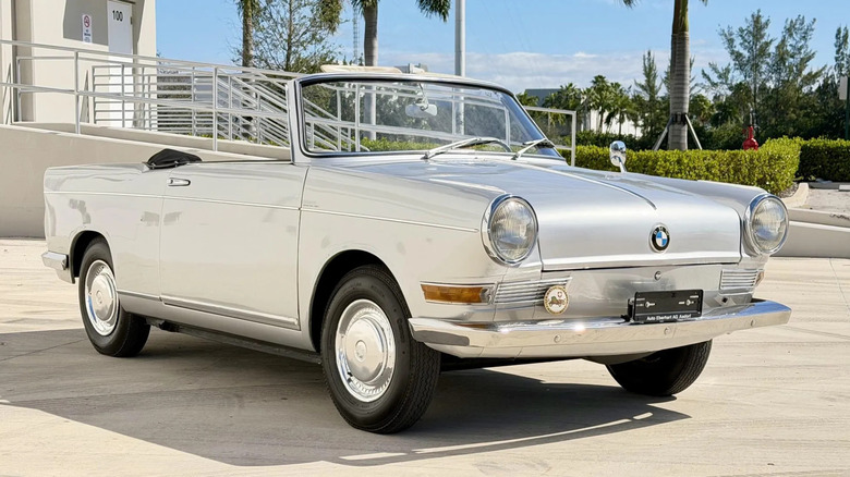Front three quarters shot of the silver BMW 700 with its top down parked in front of a loading ramp and bushes