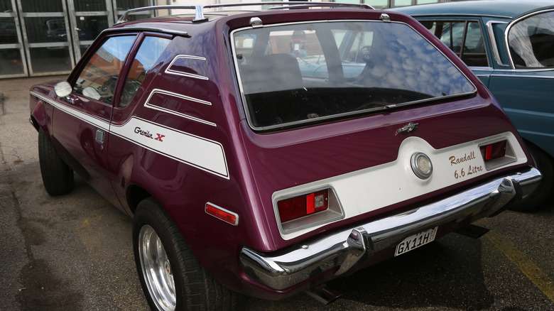 Burgundy 1972 Randall AMC Gremlin 401-XR 6.6-Litre parked next to a blue sedan on an oil-stained parking lot