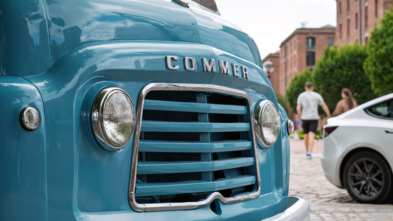 A vintage blue van on a cobblestone street parked near modern city buildings.