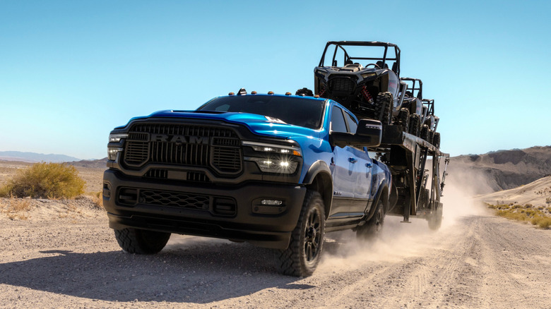 A blue Ram truck powered by a Cummins engine pulling cargo on a dirt road.