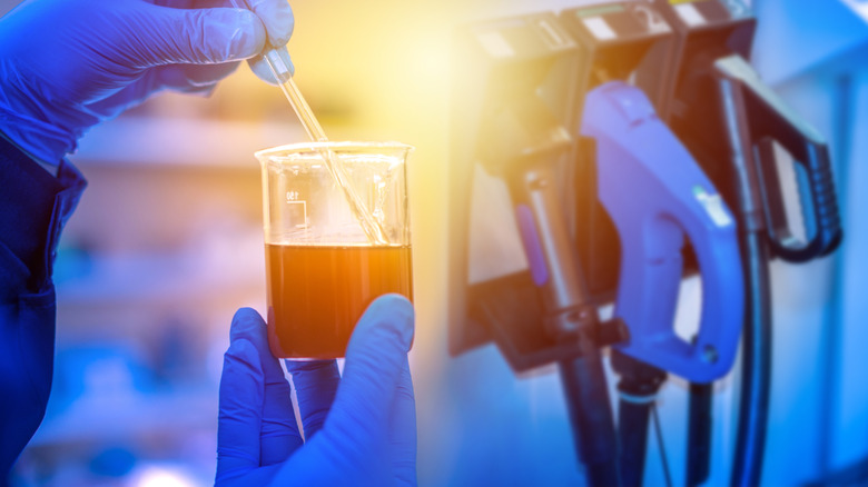 Close up of gloved hands holding beaker of liquid with gas pumps in background