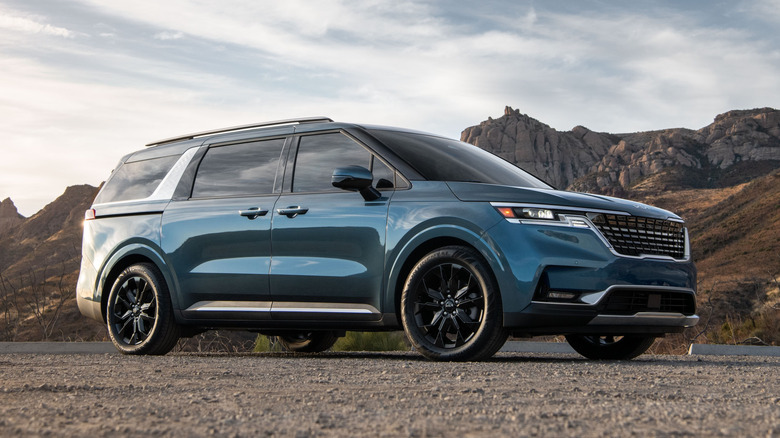A blue 2022 Kia Carnival with rocky hills in the background.
