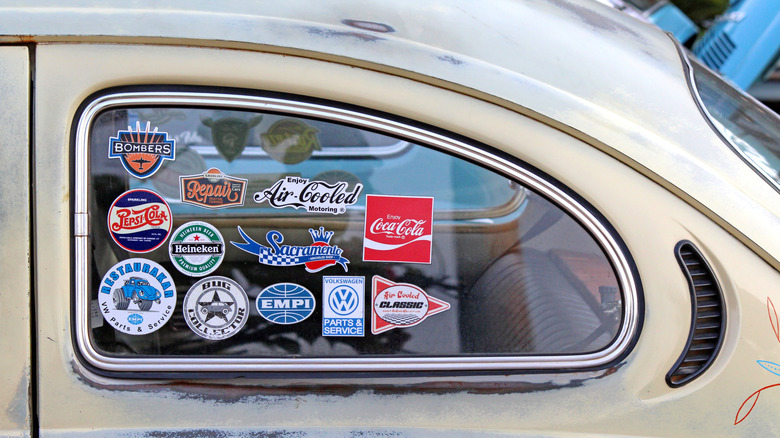 An old VW bug with multiple stickers on the rear window.