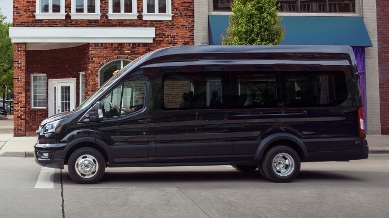 Side view of a black Ford Transit stopped at a stop sign in front of a brick building