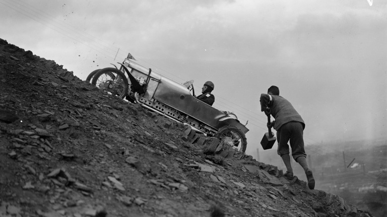 May 1927: A supporter takes a large mallet to help a competing driver up a steep, shale-covered slope in hill climbing event at Freak Hill near Bradford, Yorkshire. (Photo by Fox Photos/Getty Images)