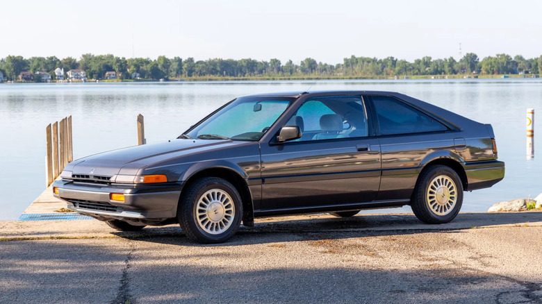 Front three-quarters shot of a gray '86 Accord hatchback parked in front of a lake