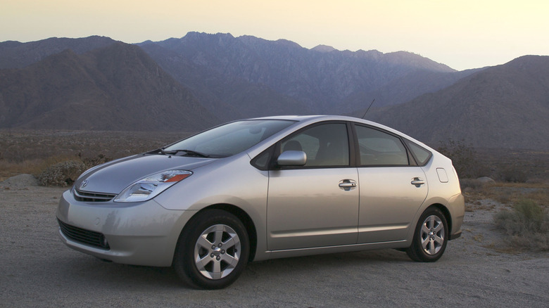 front three-quarters shot of a silver 2nd-gen Prius parked on dirt in front of a mountain skyline at dusk