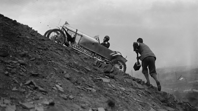 May 1927: A supporter takes a large mallet to help a competing driver up a steep, shale-covered slope in hill climbing event at Freak Hill near Bradford, Yorkshire. (Photo by Fox Photos/Getty Images)