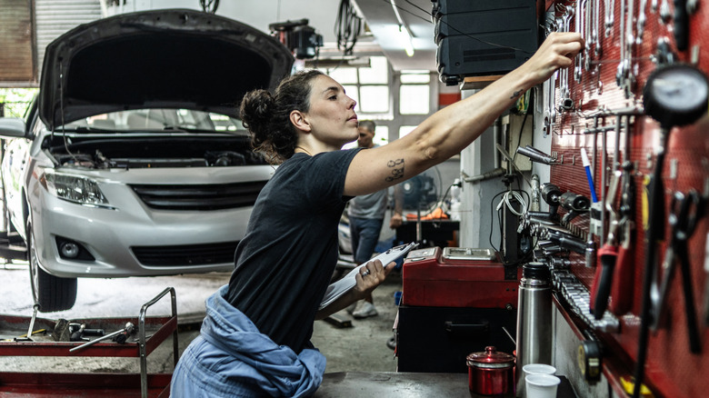 Female mechanic reaching for tools with car on lift in background
