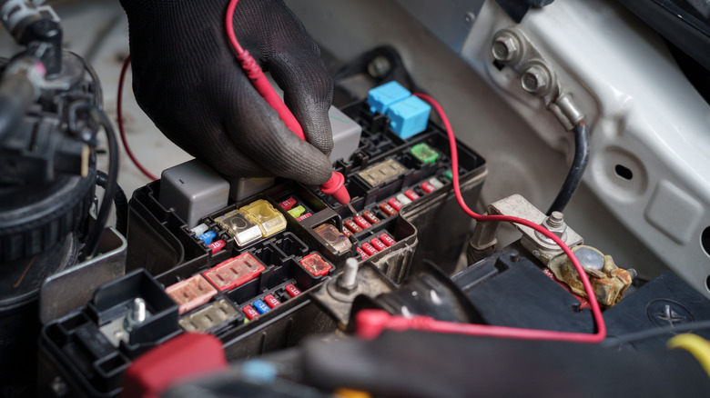 Close up of gloved hand using a multimeter to check automotive fuses