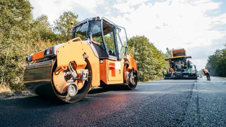 A tandem steel drum roller follows an asphalt paver during road construction