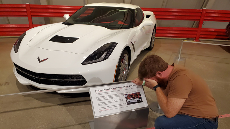 A bearded man grieves over the Corvette's last manual-transmission car in front of a white 2019 Chevrolet Corvette in the National Corvette Museum