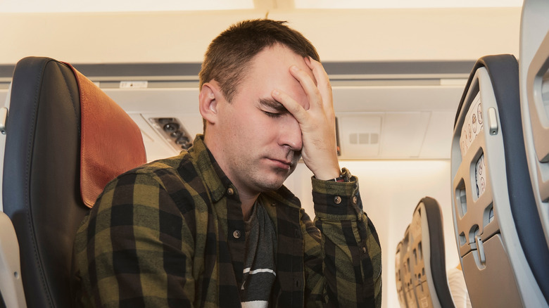 man holds his face while on a plane