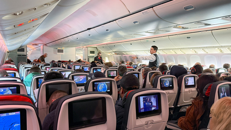 a flight attendant stands and speaks to passengers